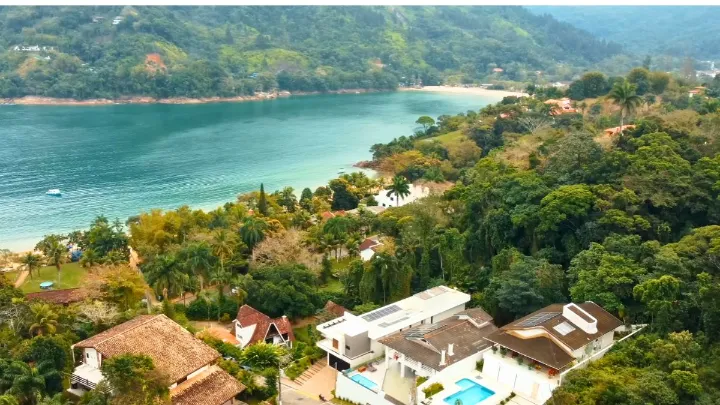 Melhores Locais para Ficar em Ubatuba Vista da praia de Ubatuba com quiosques à beira-mar e visitantes relaxando